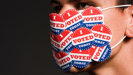 Man with face mask with many I voted today stickers. Coronavirus and American presidential elections concept.