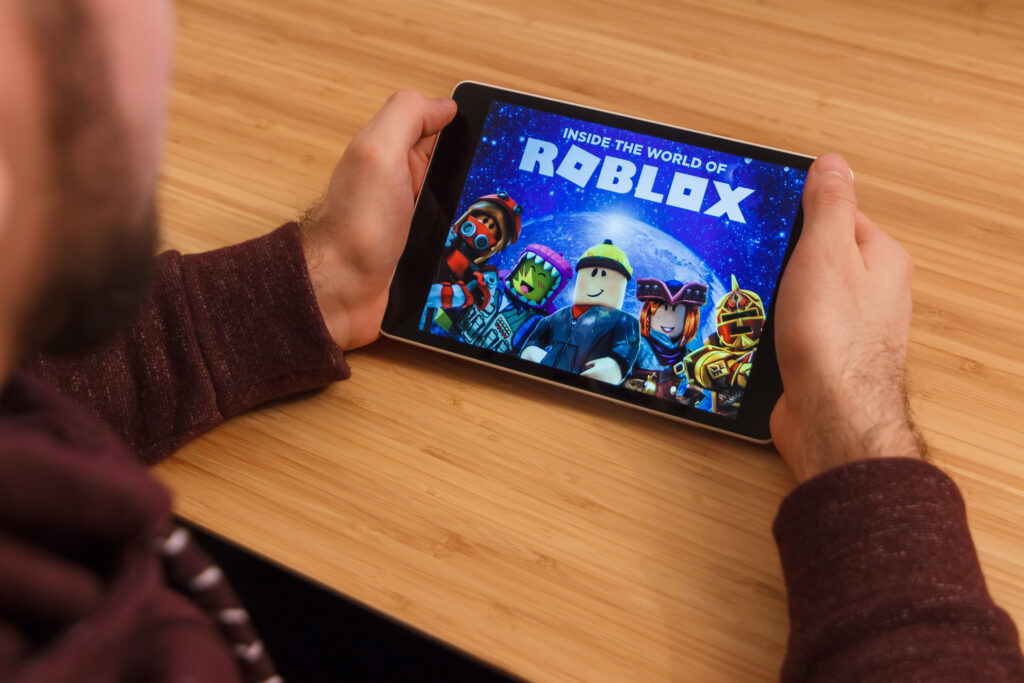 Man holding a smartphone and playng the Roblox mobile game. An illustrative editorial image on an bamboo background.