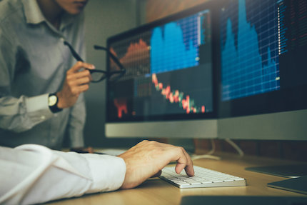 Two stock brokers looking at computer displaying financial information.