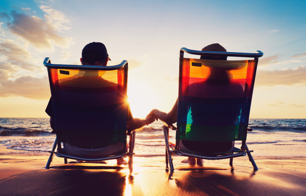 Senior couple of old man and woman sitting on the beach watching sunset