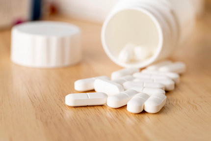 The white pills are by the medicine bottle on wooden table