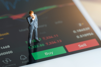 Miniature businessman standing on mobile phone showing green and yellow candlestick charts.
