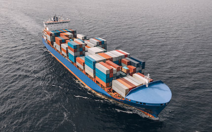 Large cargo ship loaded with shipping crates underway in ocean.