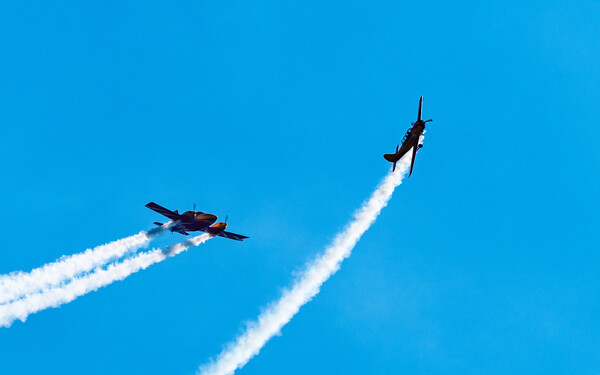 Silhouettes of training aircraft performing aerobatics on a clear sunny day.