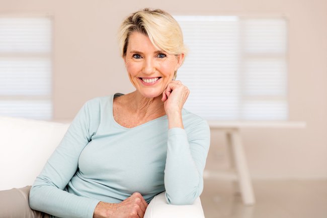 Older woman sitting on a couch smiling at the camera.