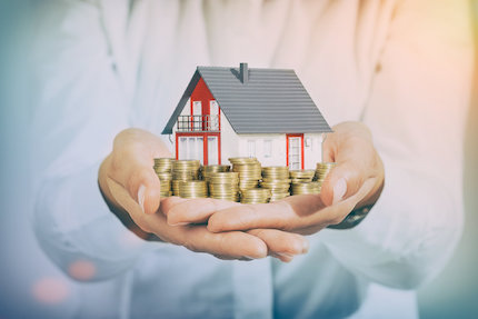 Man holding a house and gold coins in his hands.