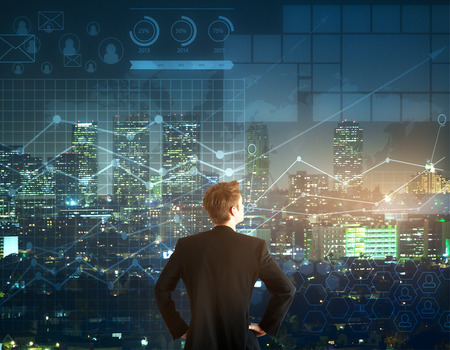 Young looking man looking at stock charts and tables superimposed over a nighttime urban landscape.
