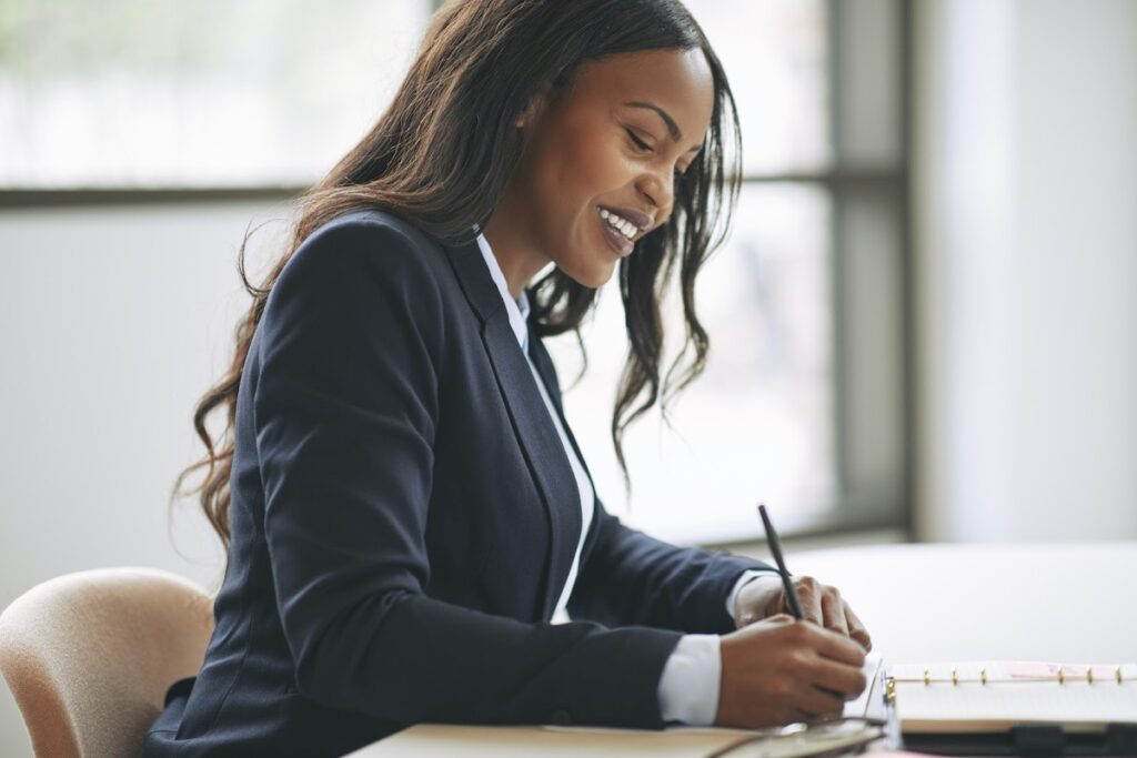 A smiling woman writing on a notepad