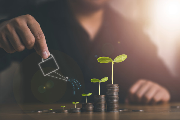 Businessman watering plants on stacks of coins