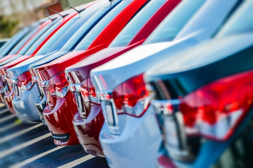 View of cars lined up at a car dealership from the perspective of the trunks.]