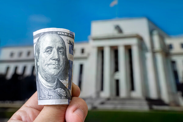 A hundred-dollar bill in front of the Federal Reserve building