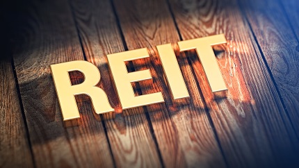 Image of the word REIT (Real Estate Investment Trust) on a wooden background