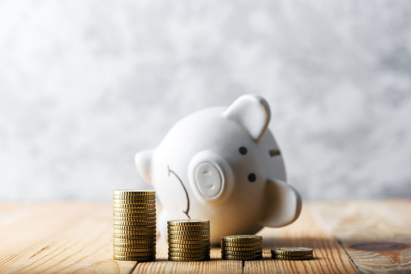 Sad piggy bank behind stacks of coins