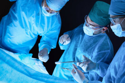 Group of surgeons at work in operating theater toned in blue. Medical team performing operation.