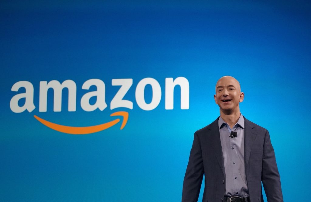 Jeff Bezos standing in from of the Amazon logo on a blue background.