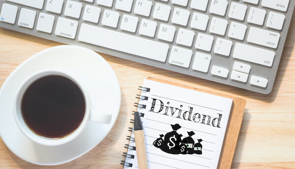 Cash dividends: dividend written in a notebook beside a cup of coffee and a keyboard