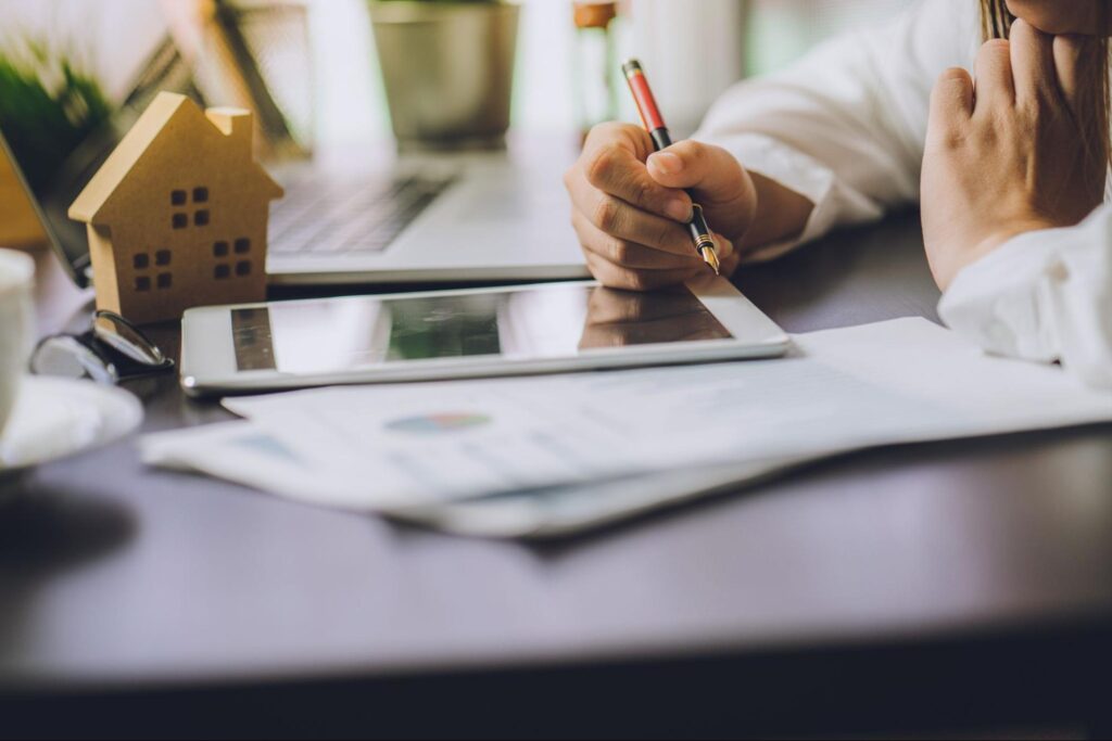 real estate stocks: Woman holding a pen while looking at her tablet and papers