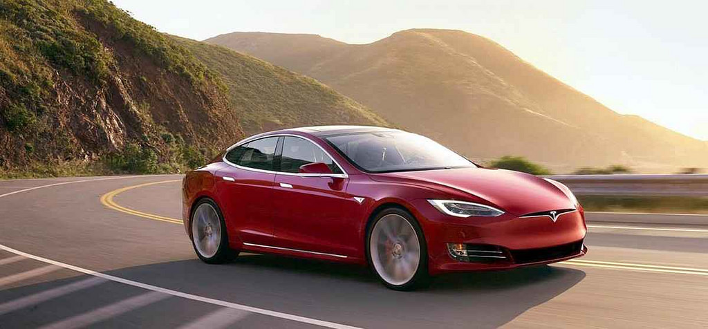 Red Tesla Model X driving on a coastal highway.