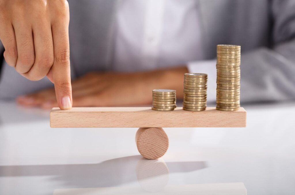 what is dividend income: Person balancing coins on top of a wooden seesaw