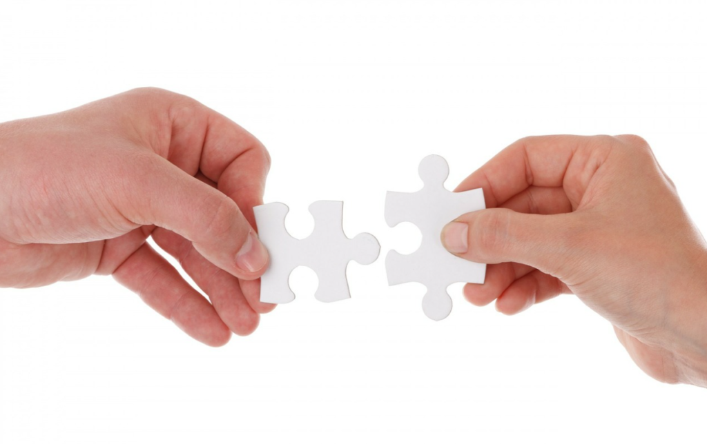 A pair of hands holding two puzzle pieces about to interlock them.