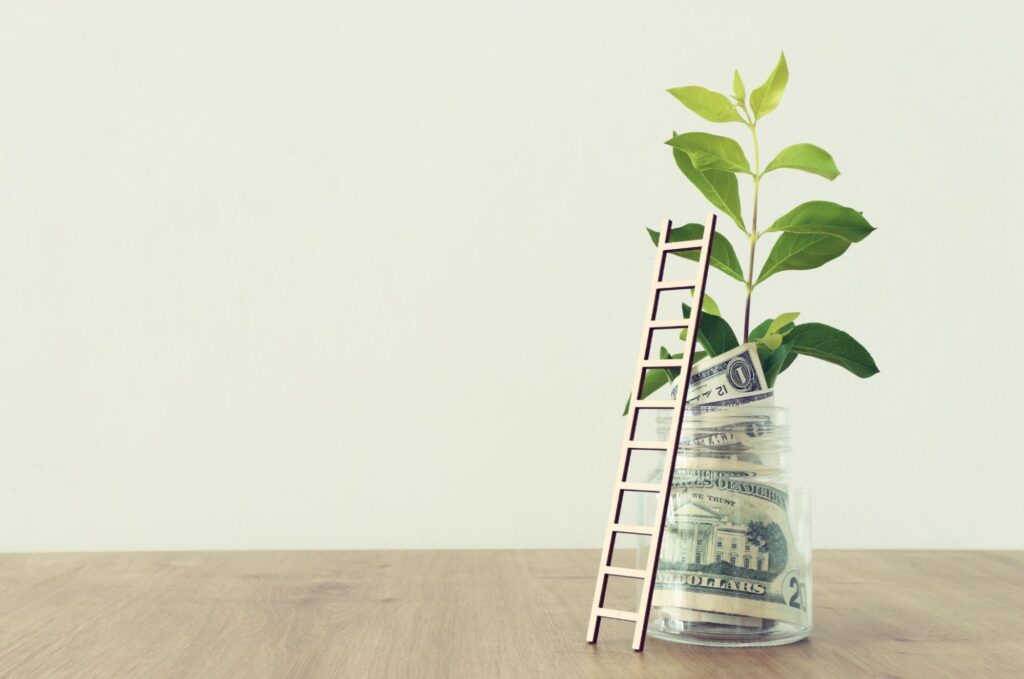 income investing: Money and a plant inside a jar with a ladder leaning against it on top of a wooden surface