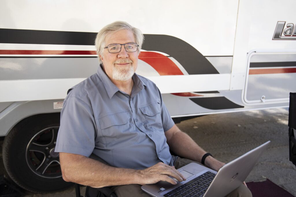 Image of Tim Plaehn sitting at laptop in front of trailer.