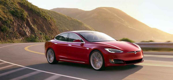 Red Tesla Model S driving on a highway at sunset.