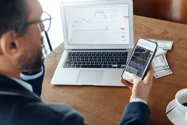 dividend rate: man looking at charts on his mobile phone and laptop