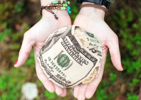 Balled $100 bills in a woman's hands indicating it's a gift.