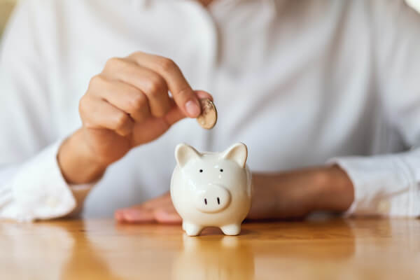 safe retirement investments: person dropping a coin in white piggy bank
