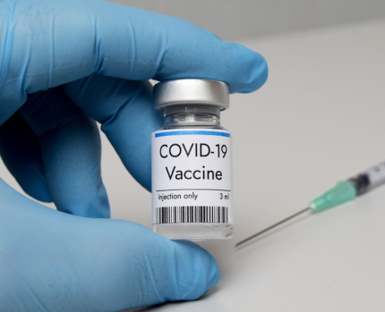 Hand wearing medical glove holding a vial of Covid-19 vaccine.