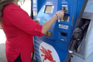 New York, USA - Circa 2018: Unidentifiable woman in red shirt swipe credit card into Mobile gas station fuel pump to pay for gasoline to fill car tank